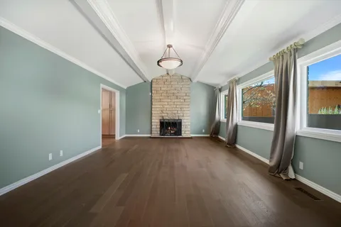 an empty room with wooden floor fireplace and windows