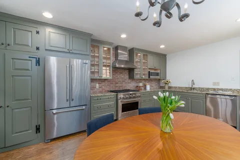 a kitchen with stainless steel appliances kitchen island granite countertop a refrigerator a stove a sink a dining table and chairs with wooden floor