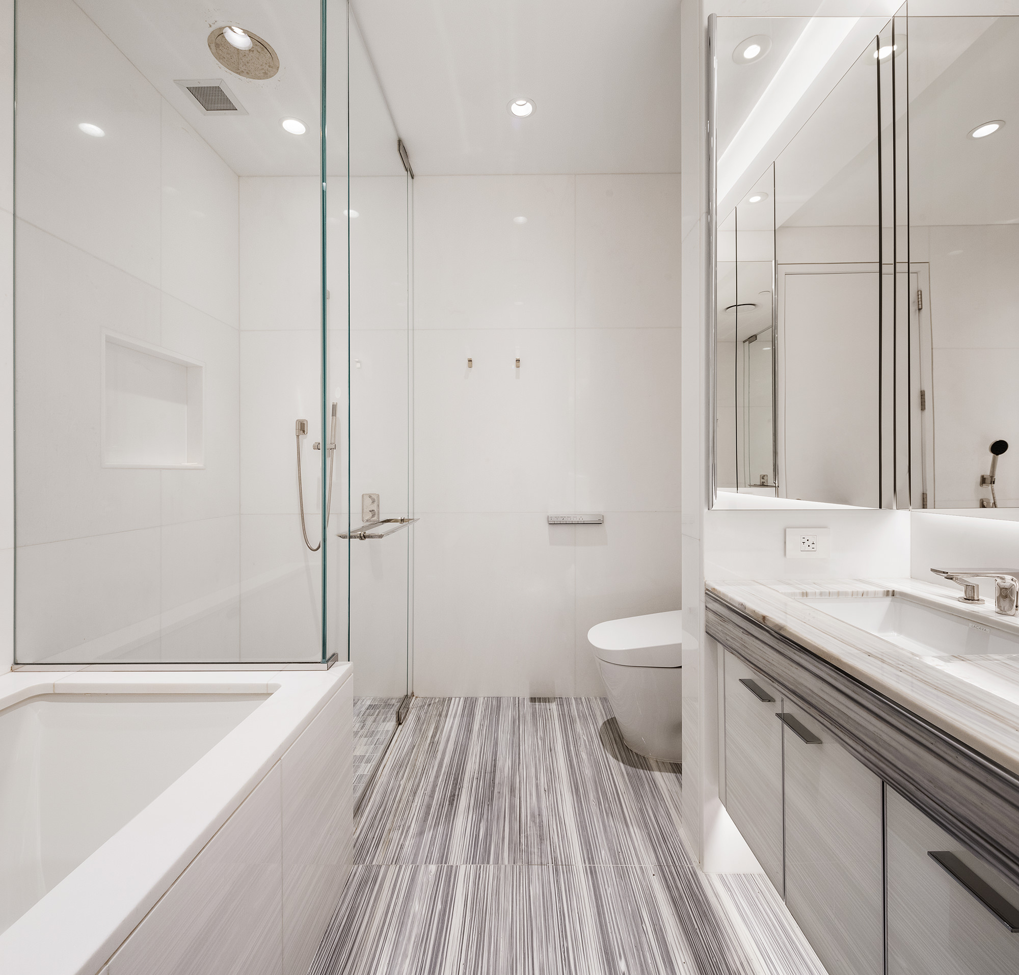 217 West 57th Street, Unit 57N Manhattan, NY 10019 - Photo 6 of 10 a bathroom with a granite countertop sink toilet a large mirror a shower and a bathtub