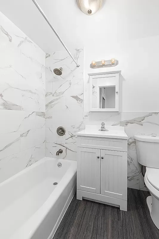 1582 York Avenue, Unit 2C Manhattan, NY 10028 - Photo 3 of 12 a bathroom with a granite countertop toilet a sink a mirror a bathtub and shower