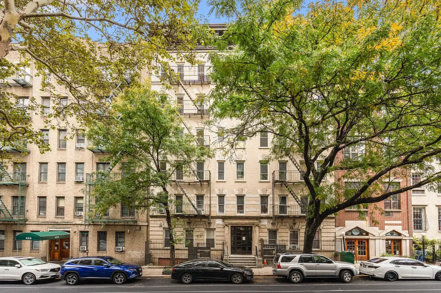 a front view of a building with lot of cars and trees