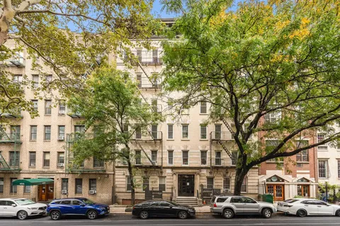 a front view of a building with lot of cars and trees