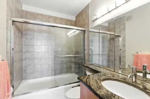 a bathroom with a granite countertop bathtub shower sink vanity and toilet
