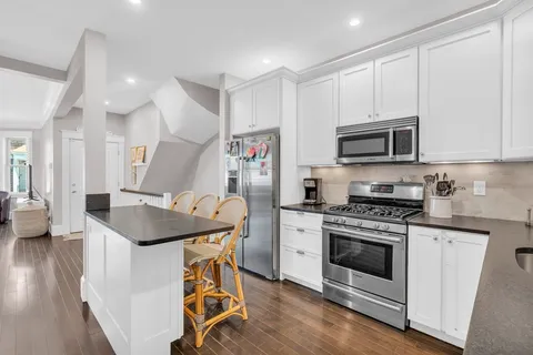 a kitchen with stainless steel appliances granite countertop a stove top oven a sink dishwasher and a refrigerator with wooden floor