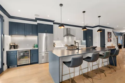 a kitchen with stainless steel appliances a sink a stove a refrigerator and chairs