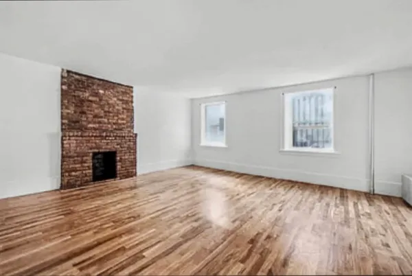 a view of an empty room with wooden floor fireplace and a window