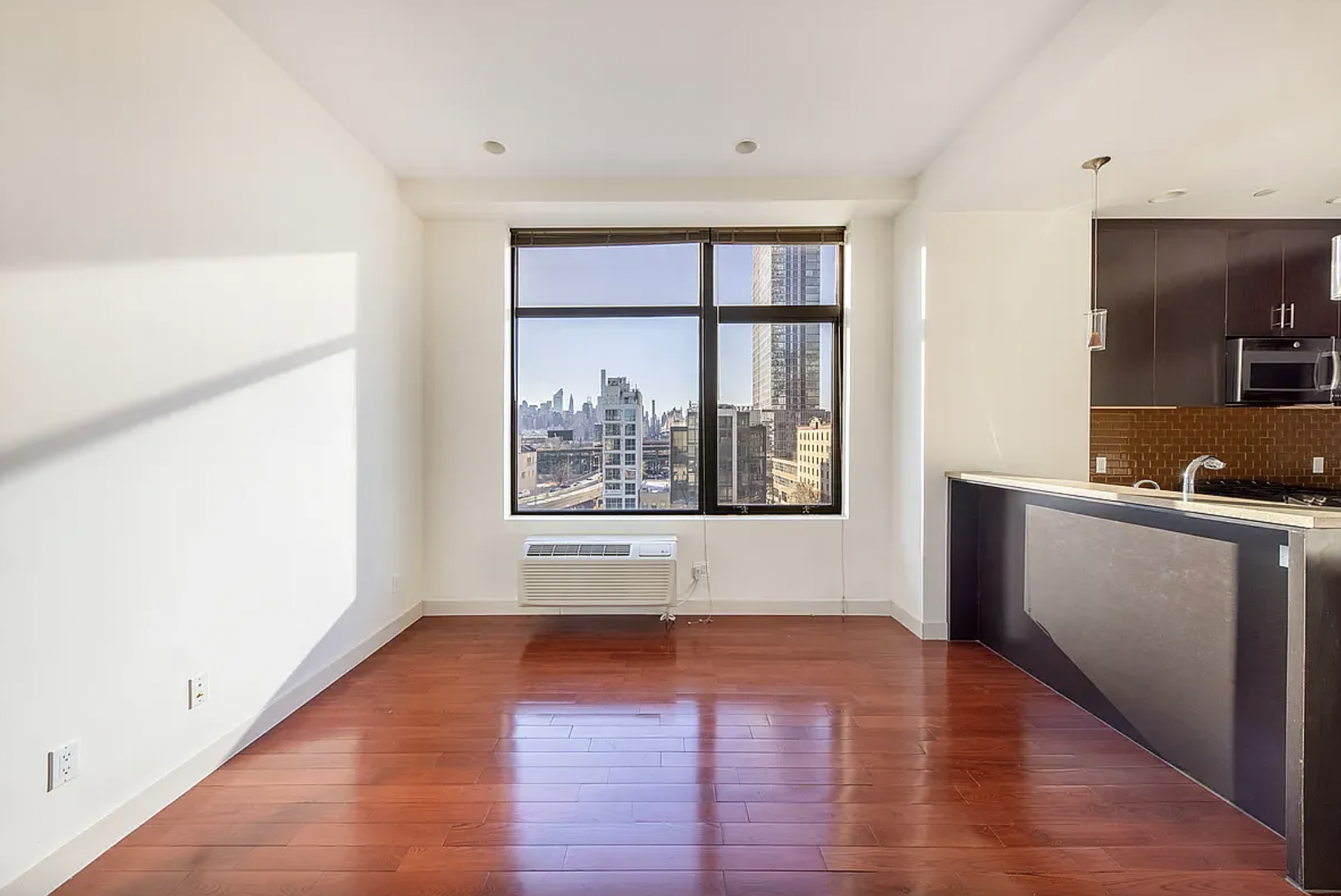 a view of an empty room with window and wooden floor