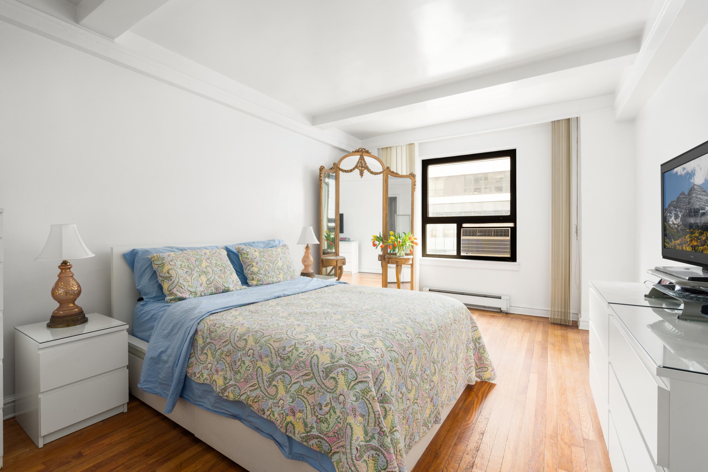 227 East 57th Street, Unit 3DEF Manhattan, NY 10022 - Photo 9 of 13 a spacious bedroom with a bed and a flat tv screen on a dresser