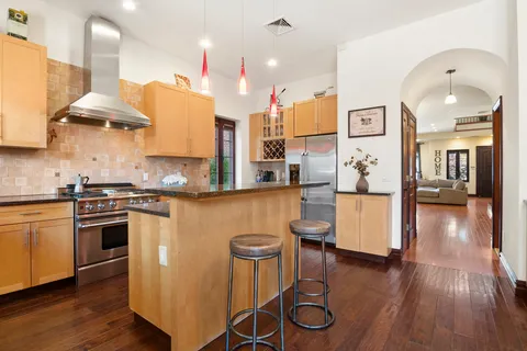 a kitchen with stainless steel appliances granite countertop a stove a sink a refrigerator and a dining table with wooden floor