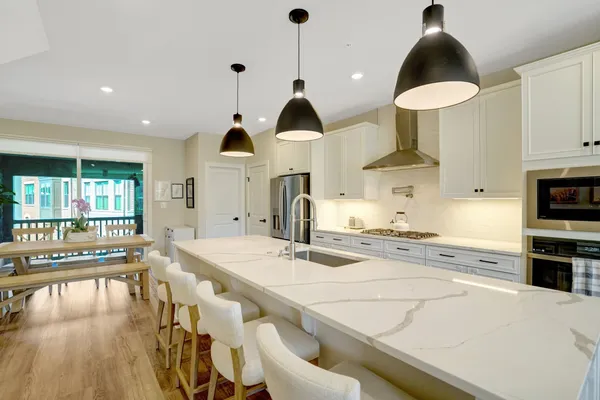 a kitchen with stainless steel appliances kitchen island granite countertop a stove a sink a refrigerator and white cabinets with wooden floor