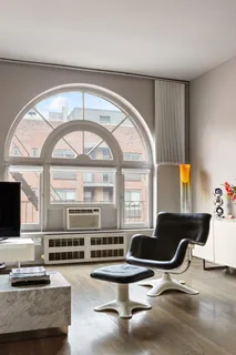 a living room with couches a flat screen tv and kitchen view with a large window