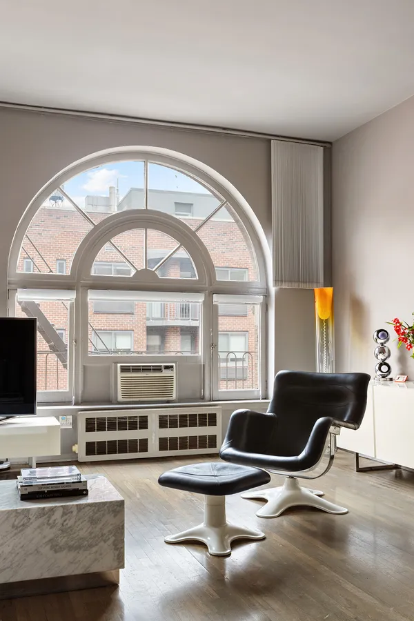 a living room with couches a flat screen tv and kitchen view with a large window