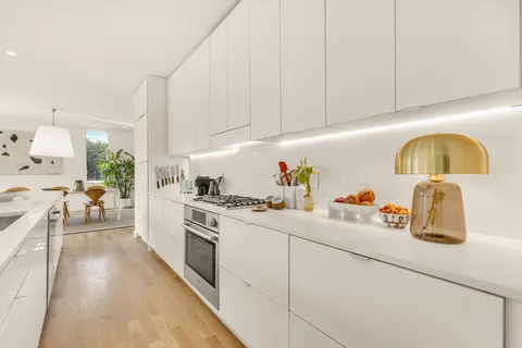 a kitchen with a sink dishwasher and white cabinets with wooden floor