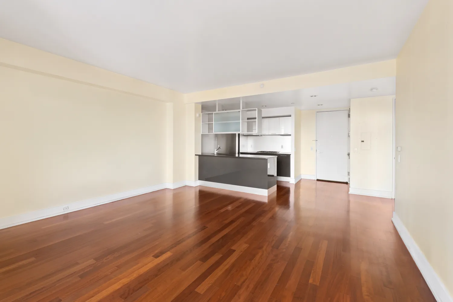 an empty room with wooden floor kitchen view and a window