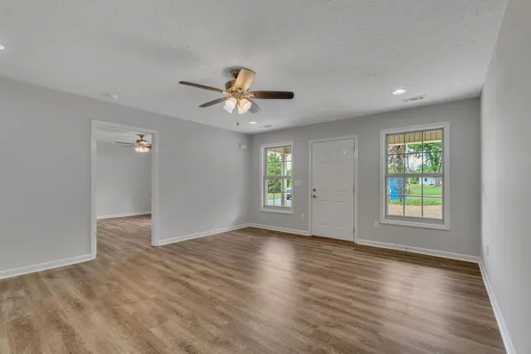 an empty room with wooden floor chandelier fan and windows
