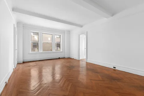 a view of an empty room with a window and wooden floor