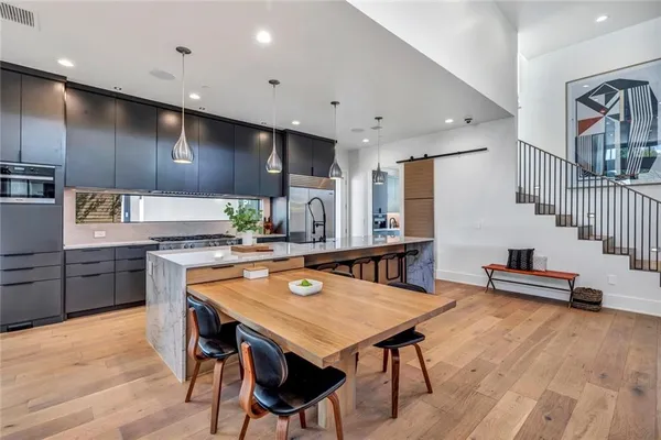 a kitchen with stainless steel appliances wooden floor dining table chairs sink and cabinets
