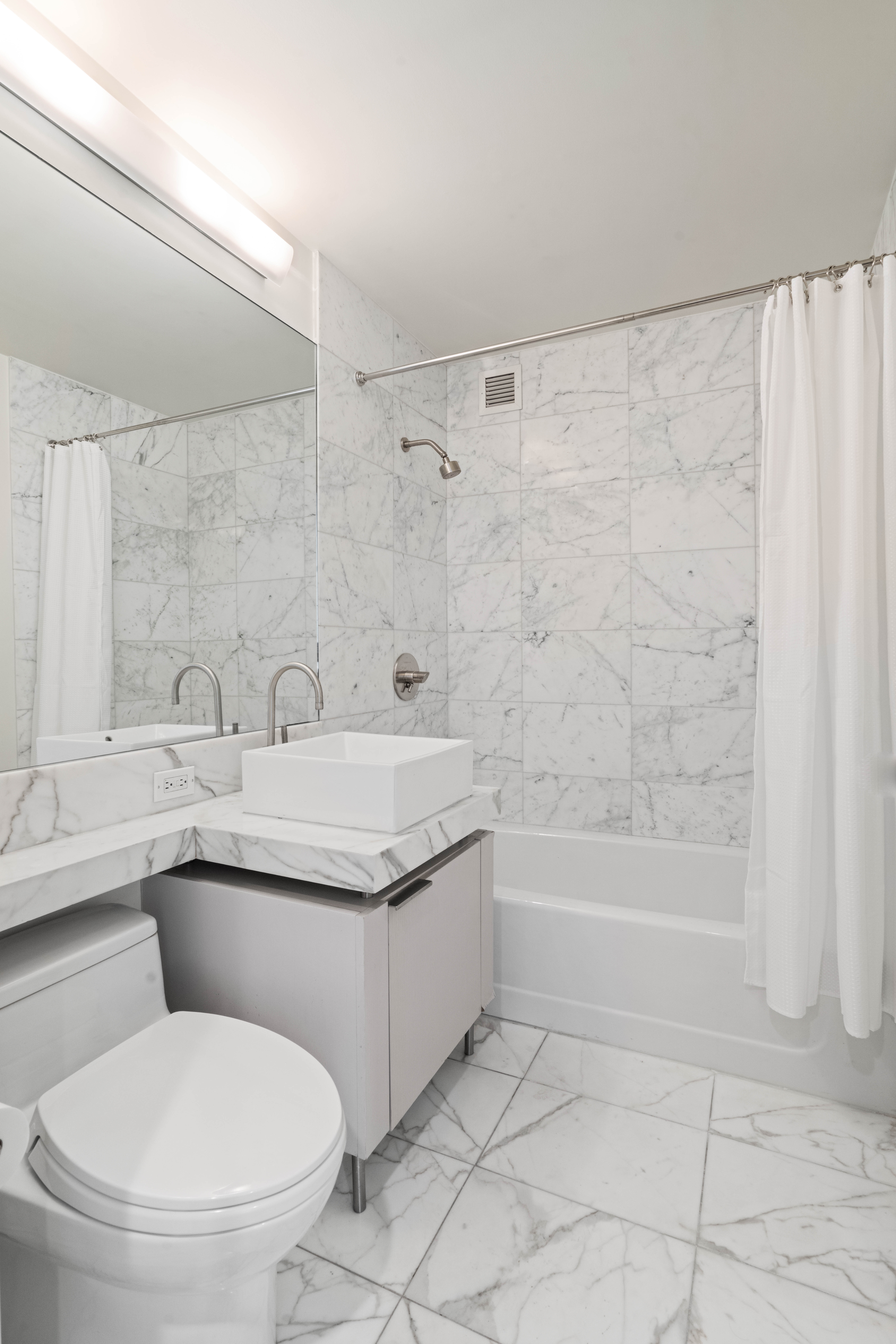 250 East 53rd Street, Unit 1402 Manhattan, NY 10022 - Photo 4 of 13 a bathroom with a granite countertop sink a toilet a mirror and a bathtub