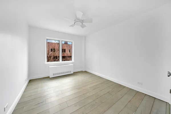 an empty room with wooden floor chandelier fan and windows