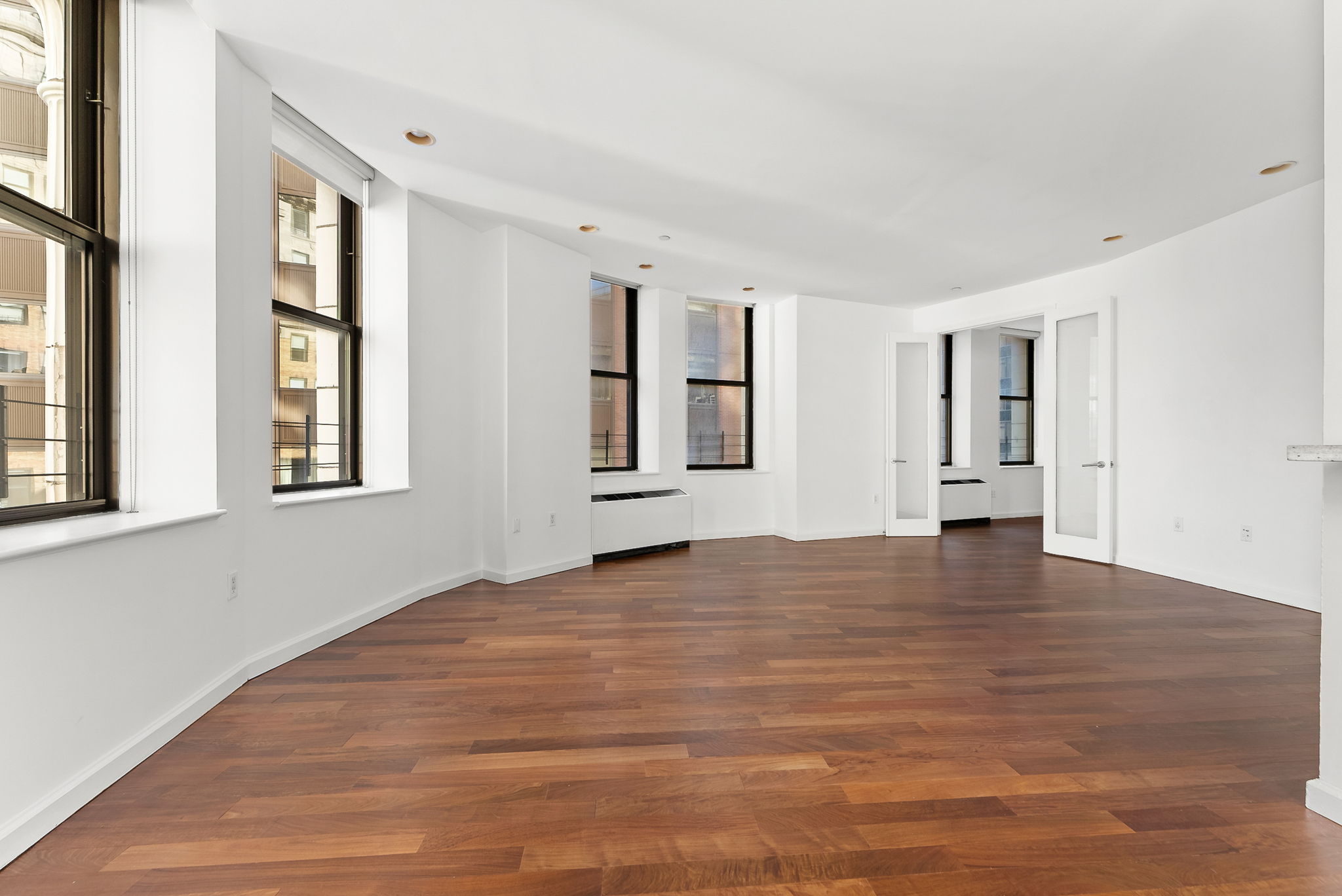 1 Wall Street Court, Unit 1405 Manhattan, NY 10005 - Photo 6 of 19 a view of an empty room with wooden floor and windows