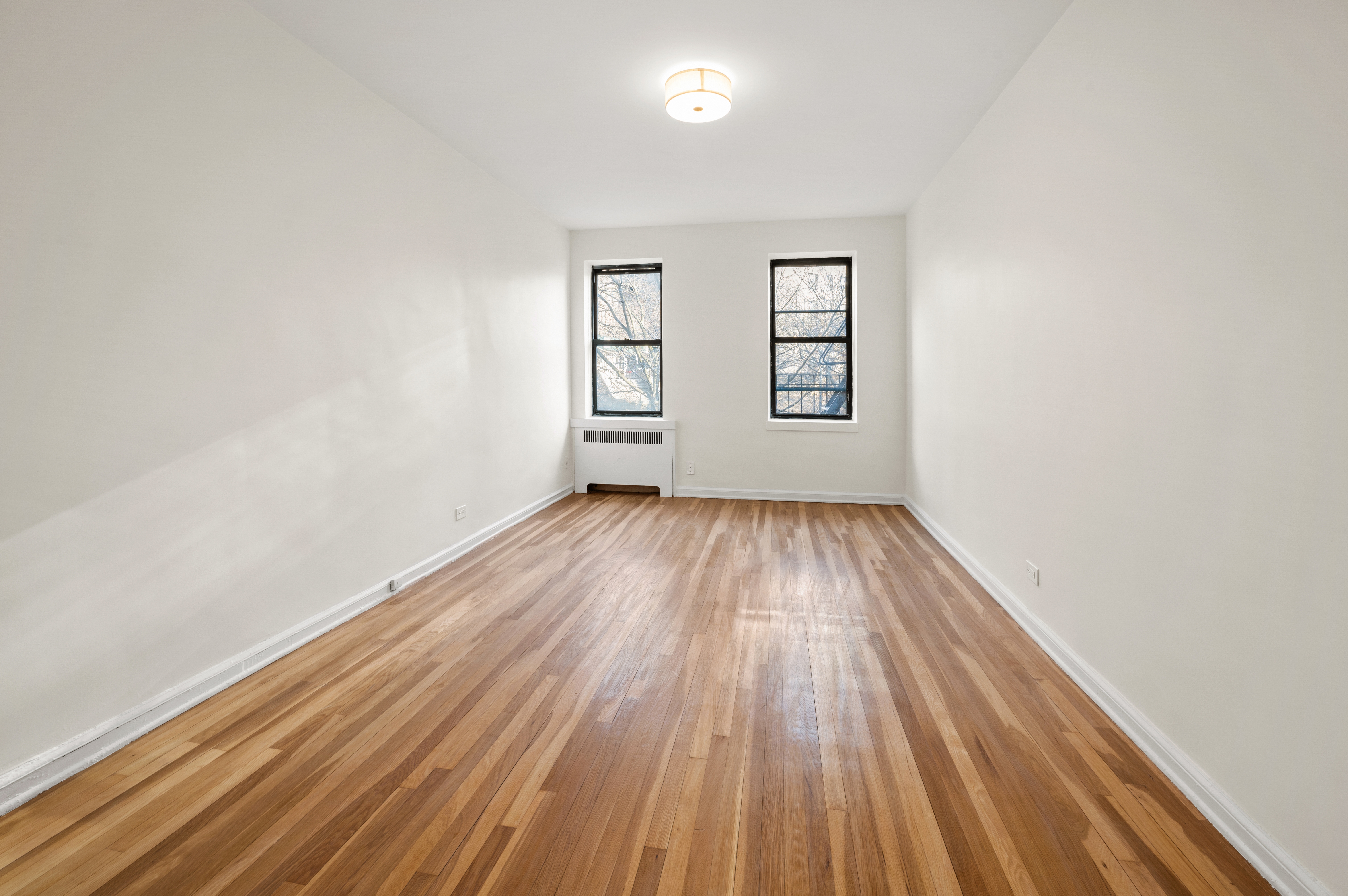 159-34 Riverside Drive West, Unit 3D Manhattan, NY 10032 - Photo 10 of 12 an empty room with wooden floor a exposed radiator and a window