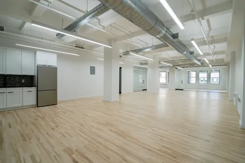a view of an empty room with wooden floor and a kitchen