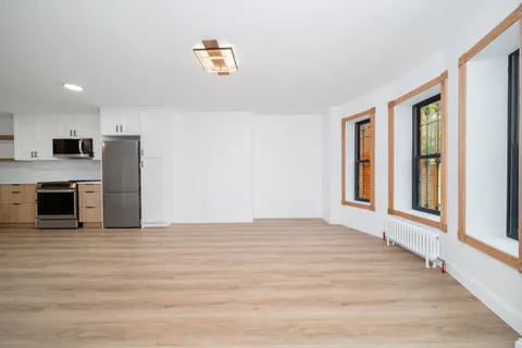 a view of an empty room with kitchen and a window