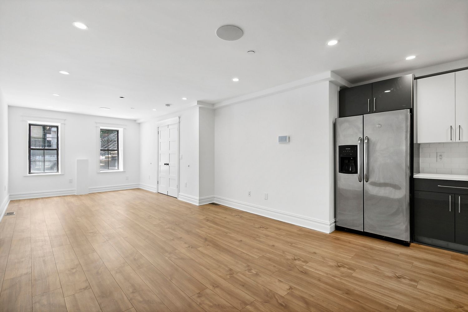 a view of an empty room with wooden floor and a kitchen