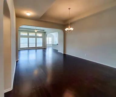 an empty room with wooden floor chandelier and windows