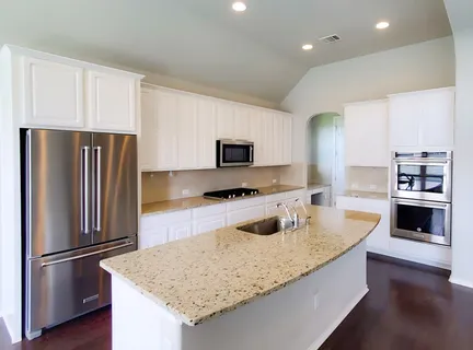 a kitchen with granite countertop a refrigerator oven a sink dishwasher and white cabinets with wooden floor