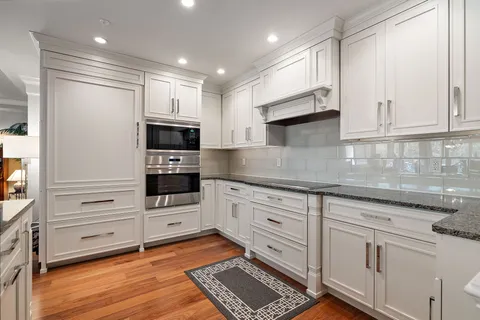a kitchen with stainless steel appliances kitchen island granite countertop a stove and white cabinets with wooden floor