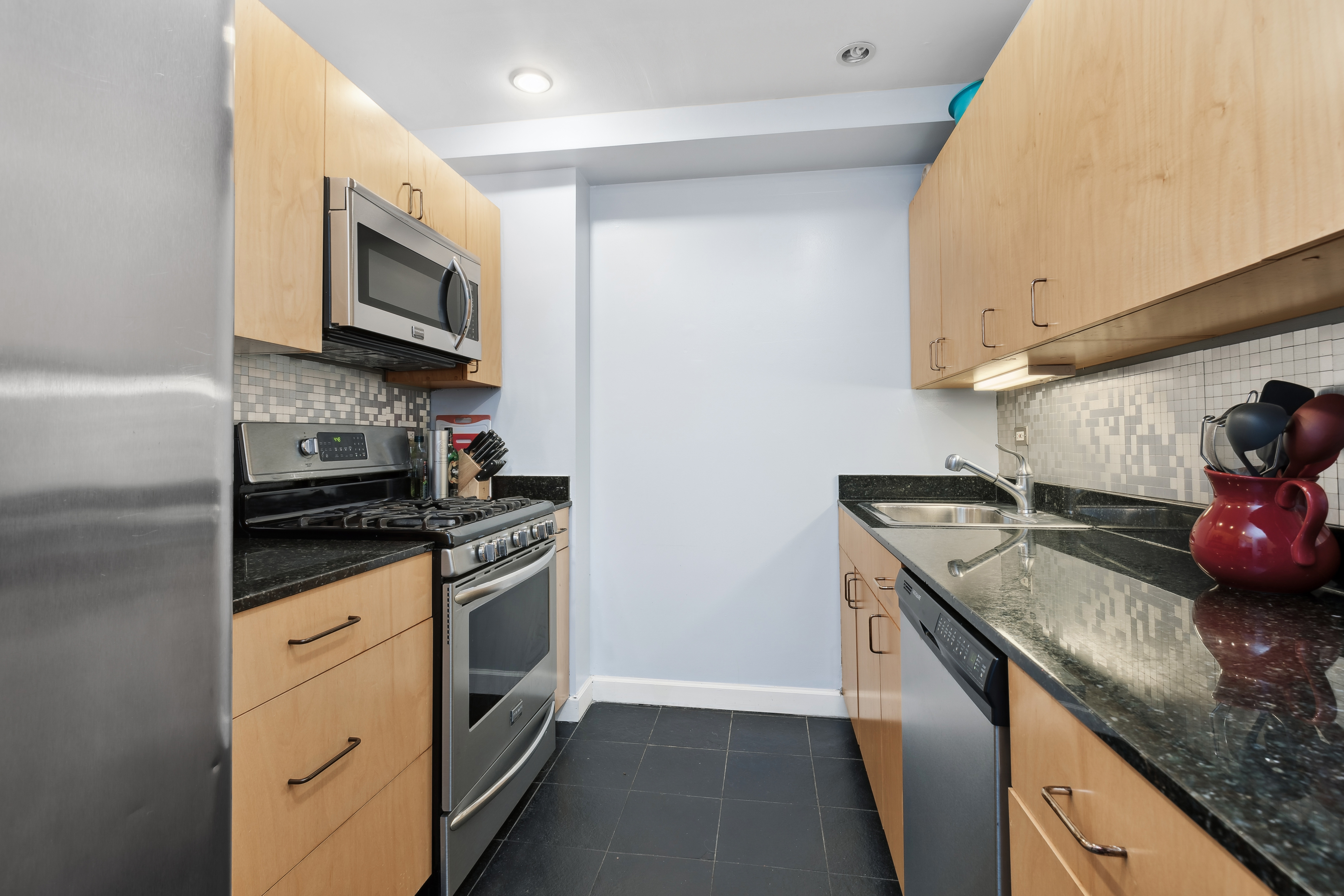 1400 5th Avenue, Unit 8J Manhattan, NY 10026 - Photo 2 of 8 a kitchen with granite countertop a sink stainless steel appliances and white cabinets
