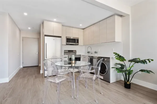 a view of kitchen with stainless steel appliances a dining table chairs refrigerator and microwave