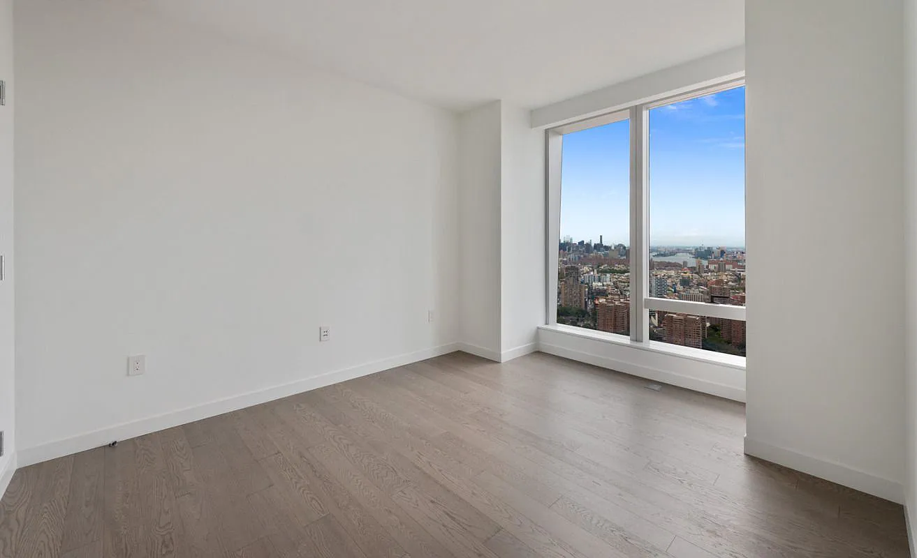 252 South Street, Unit 52J Manhattan, NY 10002 - Photo 6 of 17 an empty room with wooden floor and windows