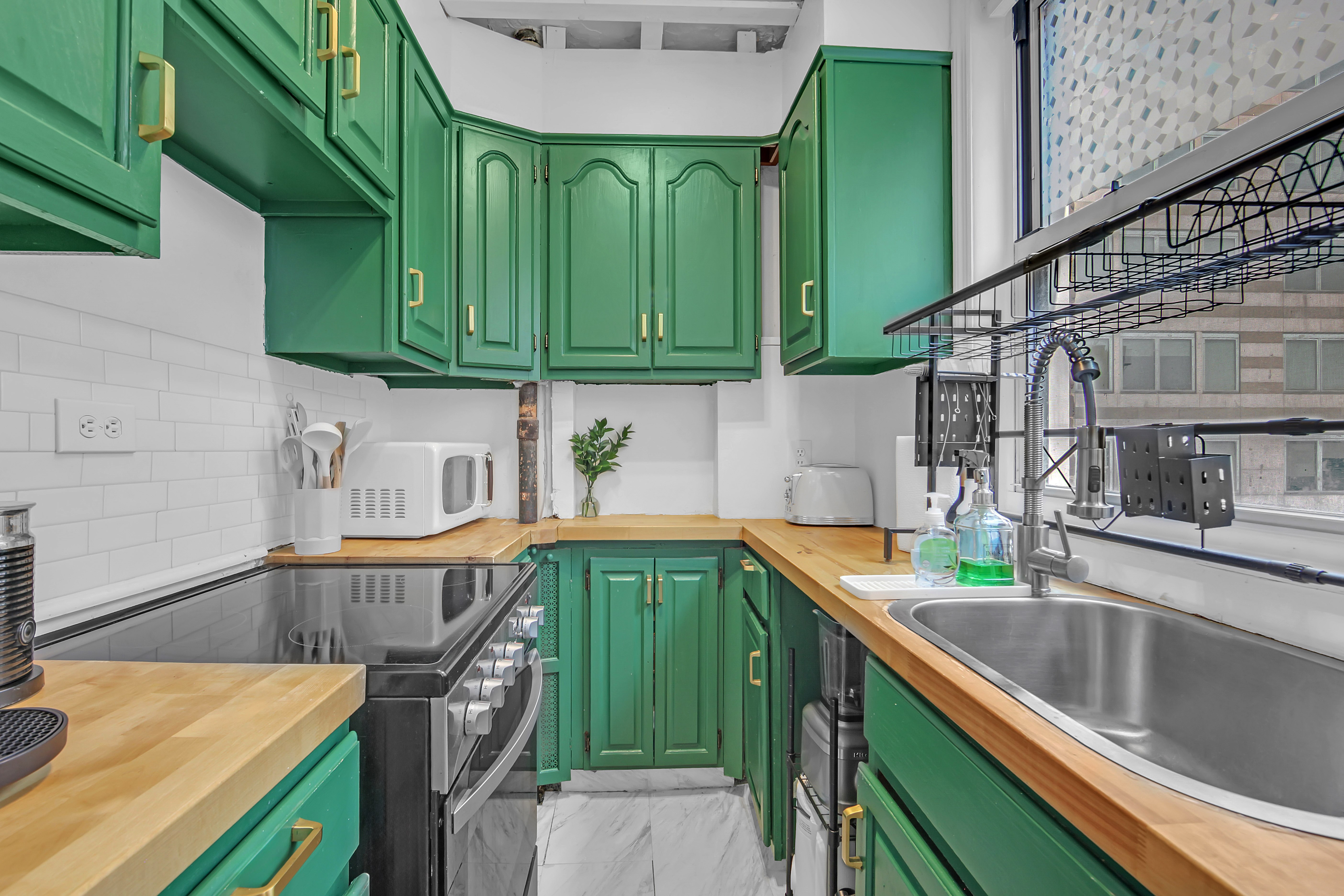 333 East 43rd Street, Unit 909 Manhattan, NY 10017 - Photo 3 of 22 a kitchen with green cabinets a sink and a stove top oven