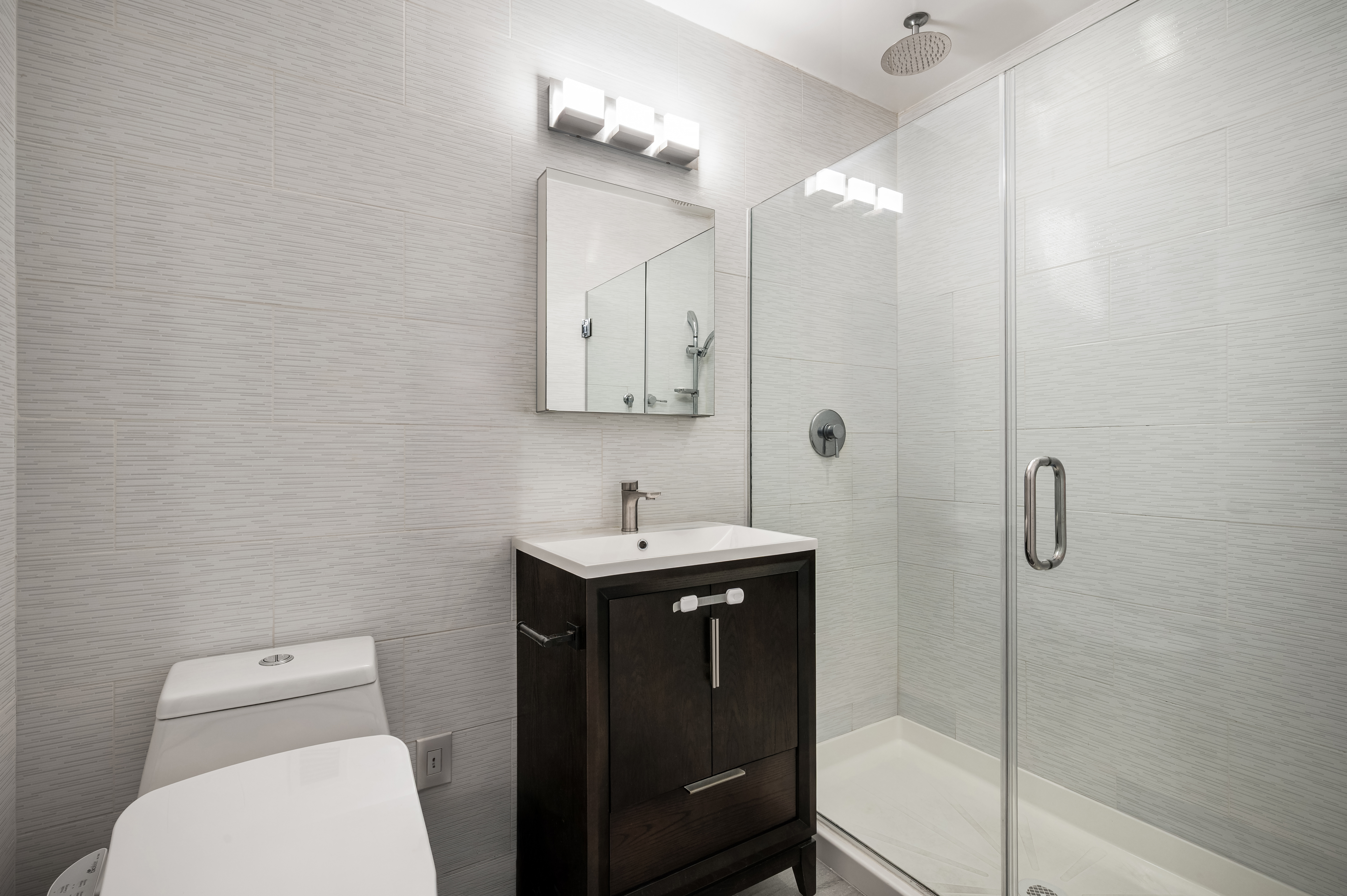 41-26 27th Street, Unit 5E Queens, NY 11101 - Photo 4 of 12 a bathroom with a toilet a sink a shower a mirror and vanity