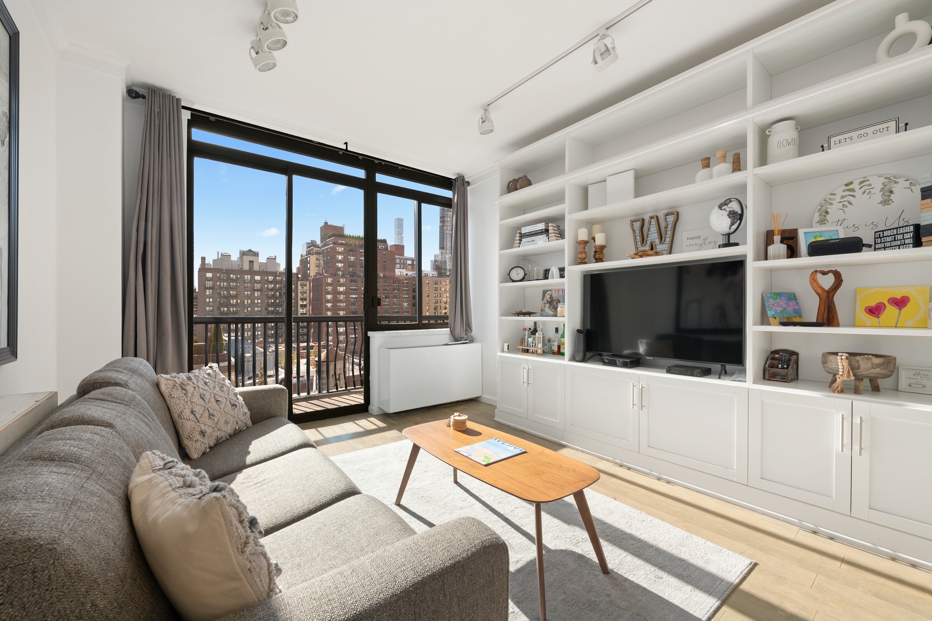 343 East 74th Street, Unit 14K Manhattan, NY 10021 - Photo 2 of 7 a living room with furniture a flat screen tv and a floor to ceiling window