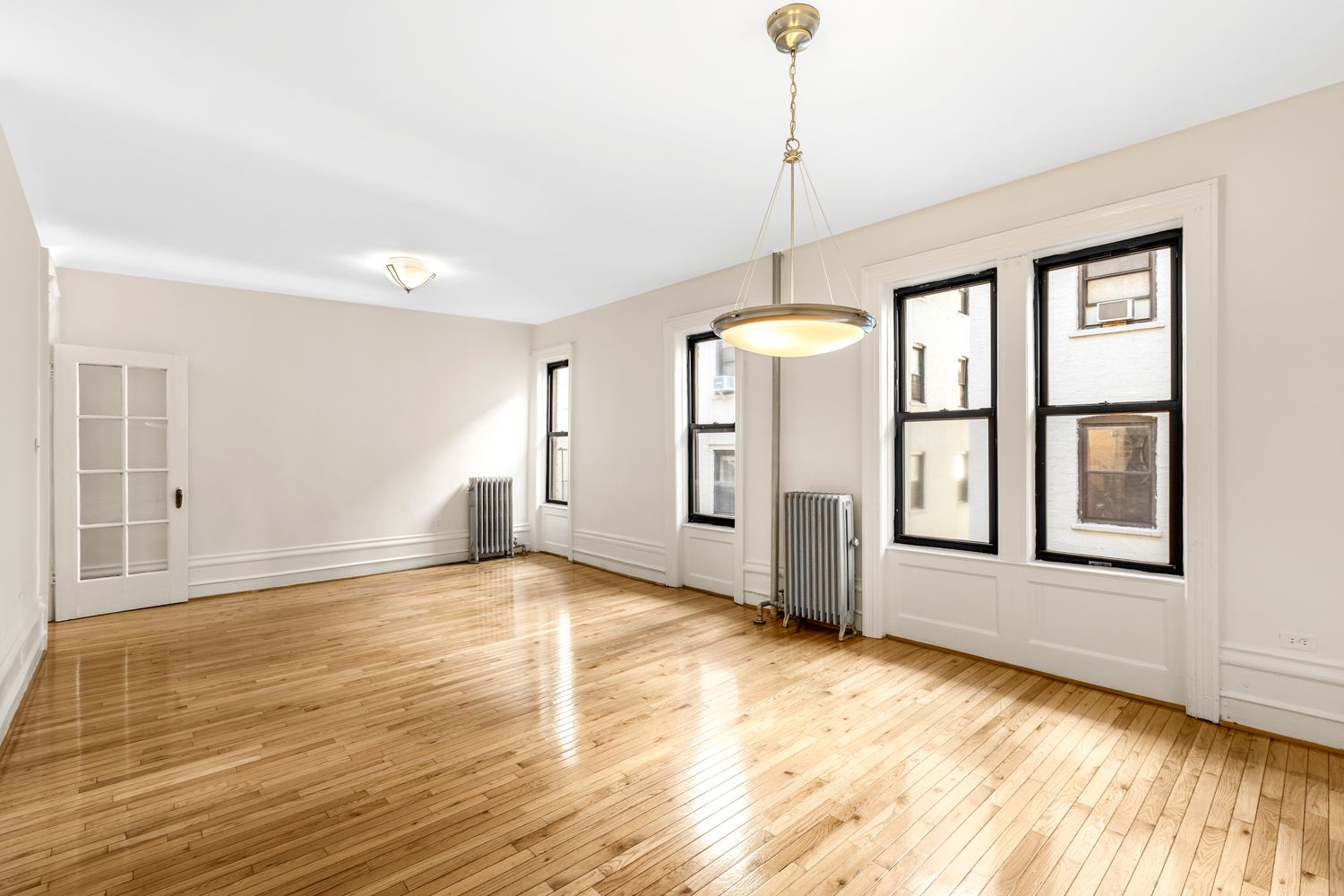 a view of an empty room with window and wooden floor
