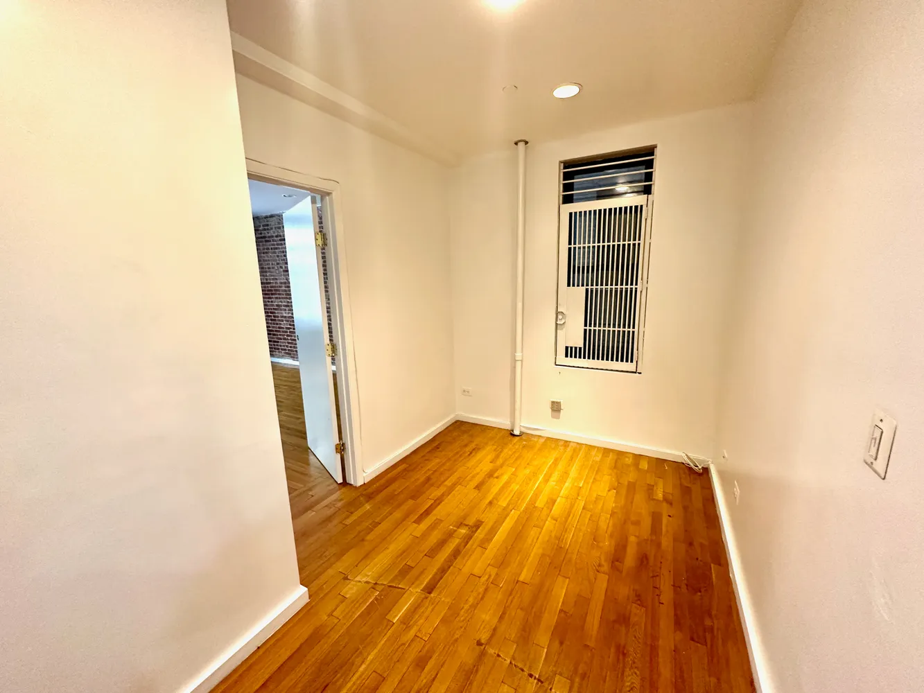 a view of an empty room with wooden floor and a window