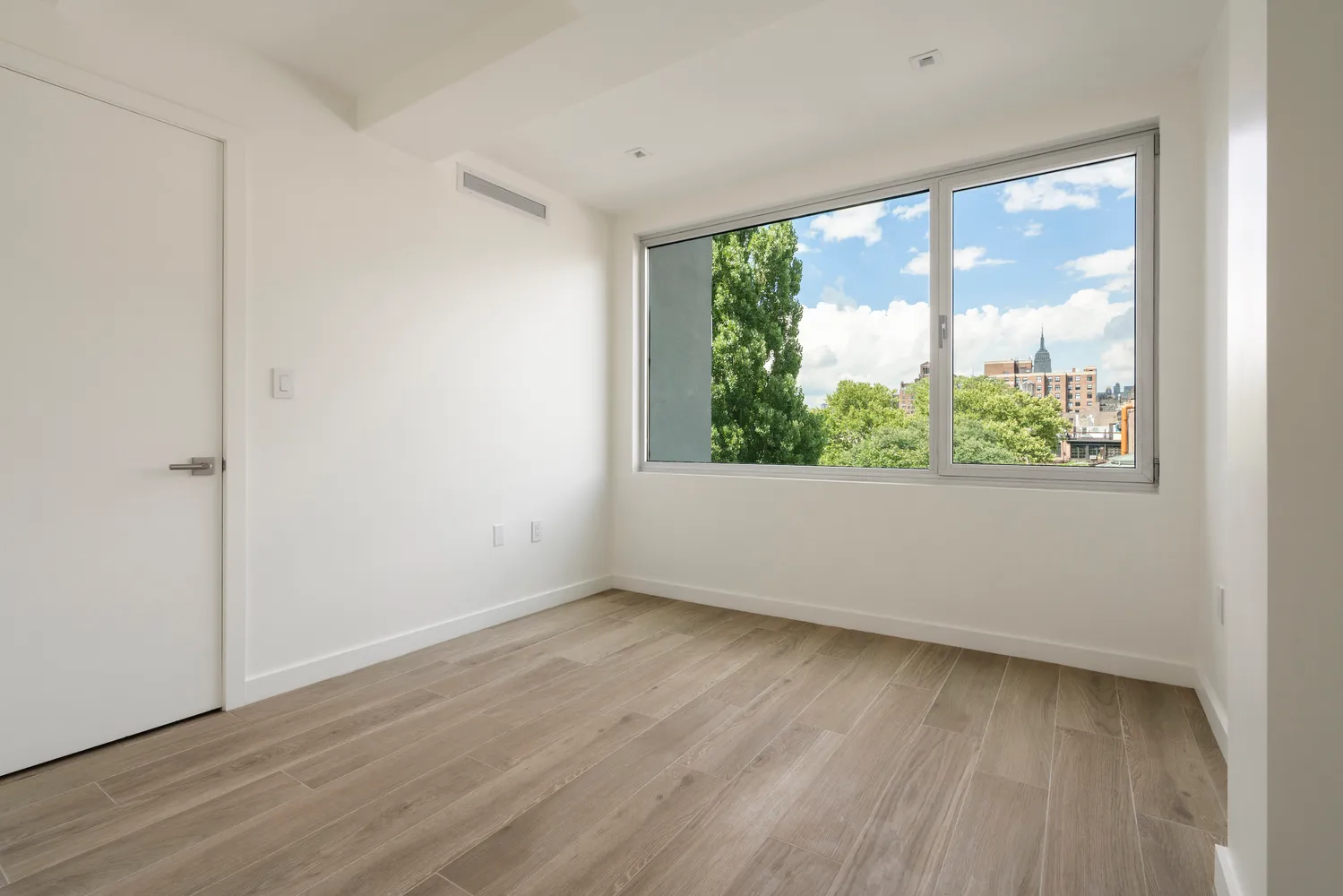 a view of an empty room with wooden floor and a window
