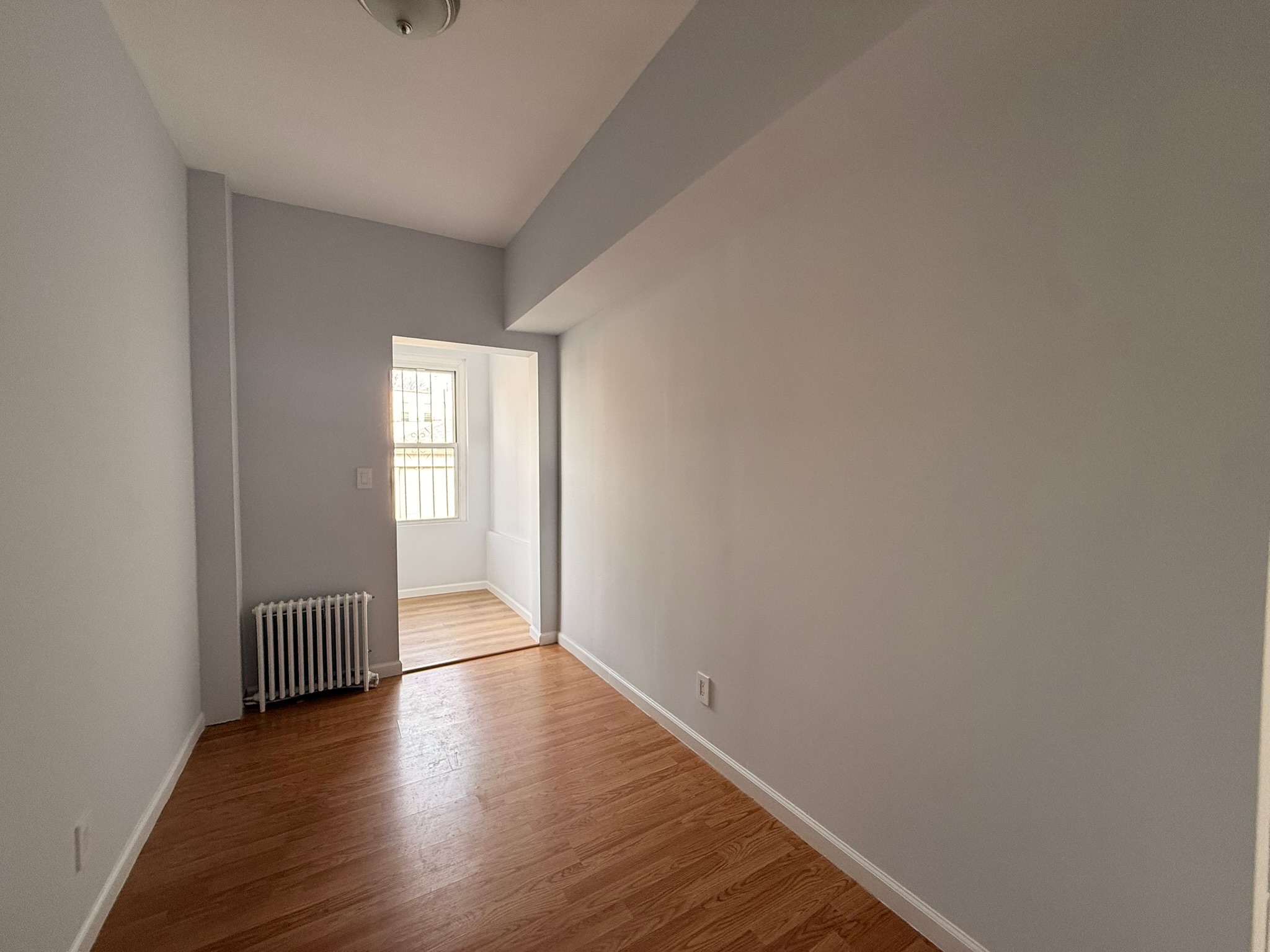 1675 85th Street, Unit 1R Brooklyn, NY 11214 - Photo 5 of 8 a view of an empty room with wooden floor and a window