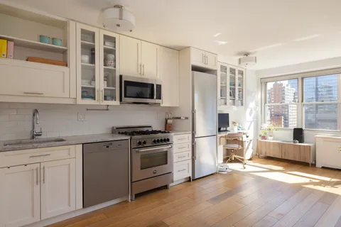 a kitchen with stainless steel appliances a stove top oven a refrigerator a sink and white cabinets with wooden floor