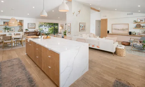 a large living room with stainless steel appliances kitchen island granite countertop a refrigerator a sink and white cabinets