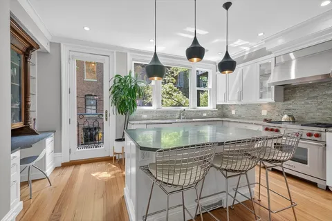 a kitchen with stainless steel appliances granite countertop a stove top oven a sink a dining table and chairs with wooden floor