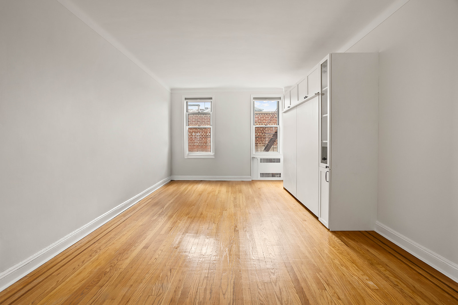 76-12 35th Avenue, Unit 6J Queens, NY 11372 - Photo 5 of 17 an empty room with wooden floor and windows