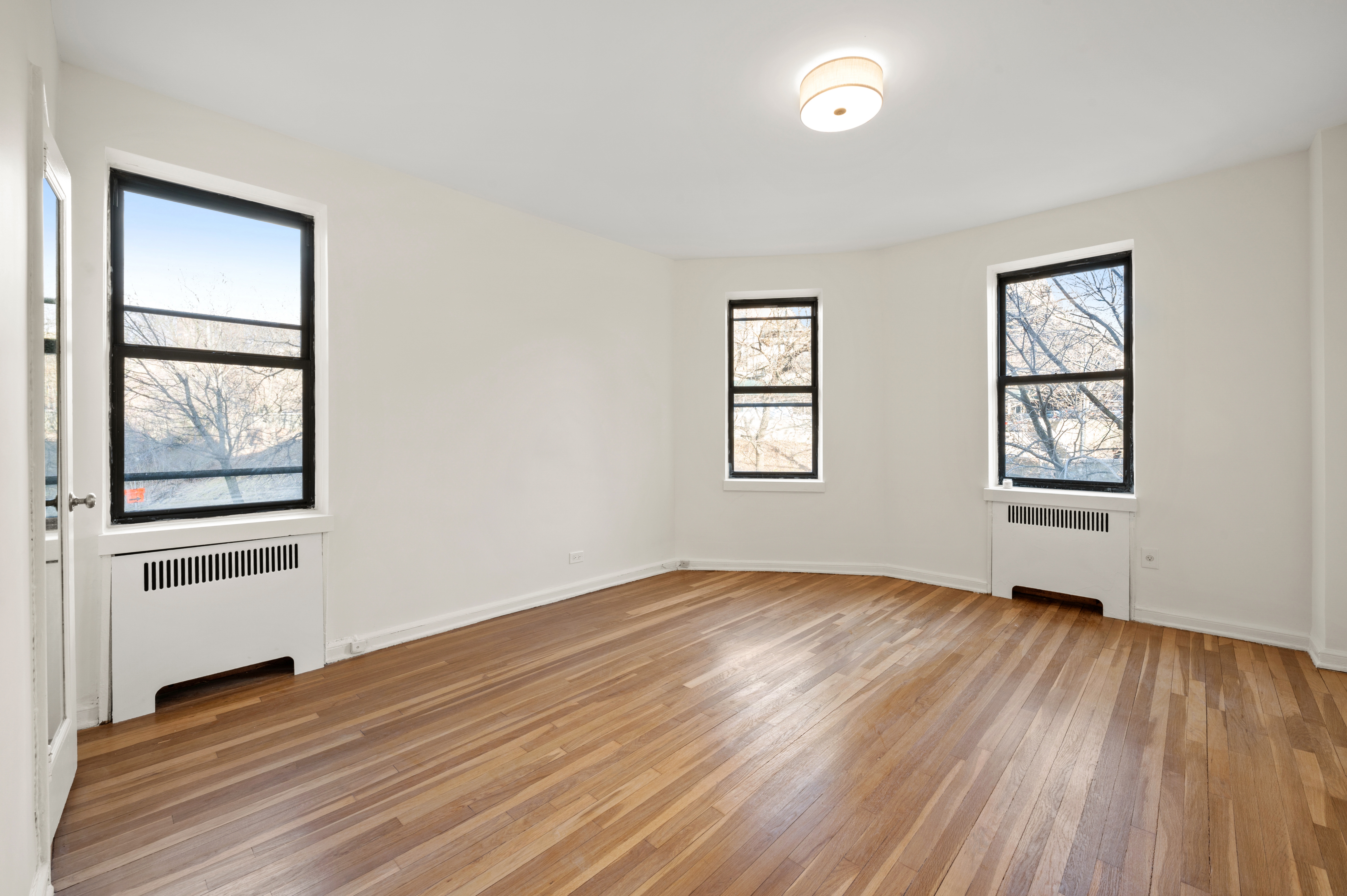 159-34 Riverside Drive West, Unit 3D Manhattan, NY 10032 - Photo 8 of 12 an empty room with wooden floor and windows
