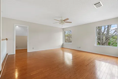 an empty room with wooden floor chandelier fan and windows