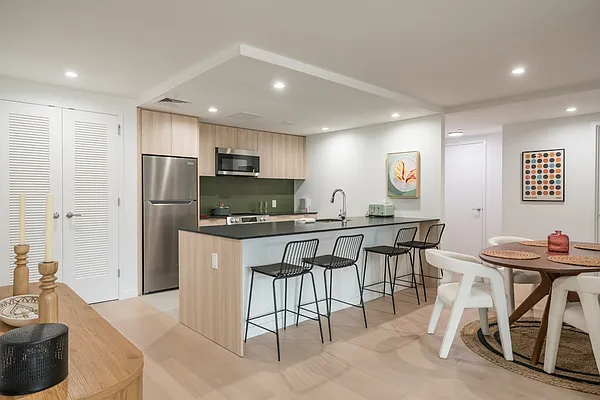 a kitchen with stainless steel appliances kitchen island granite countertop a dining table chairs and a refrigerator
