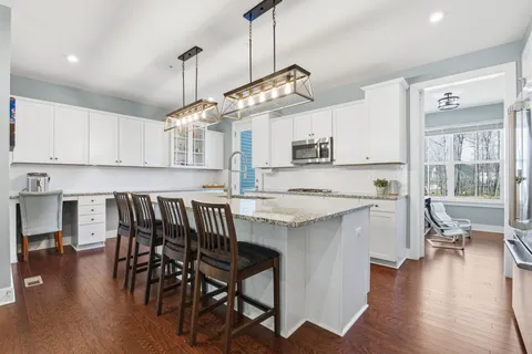 a kitchen with stainless steel appliances granite countertop a stove top oven a refrigerator a dining table and chairs with wooden floor