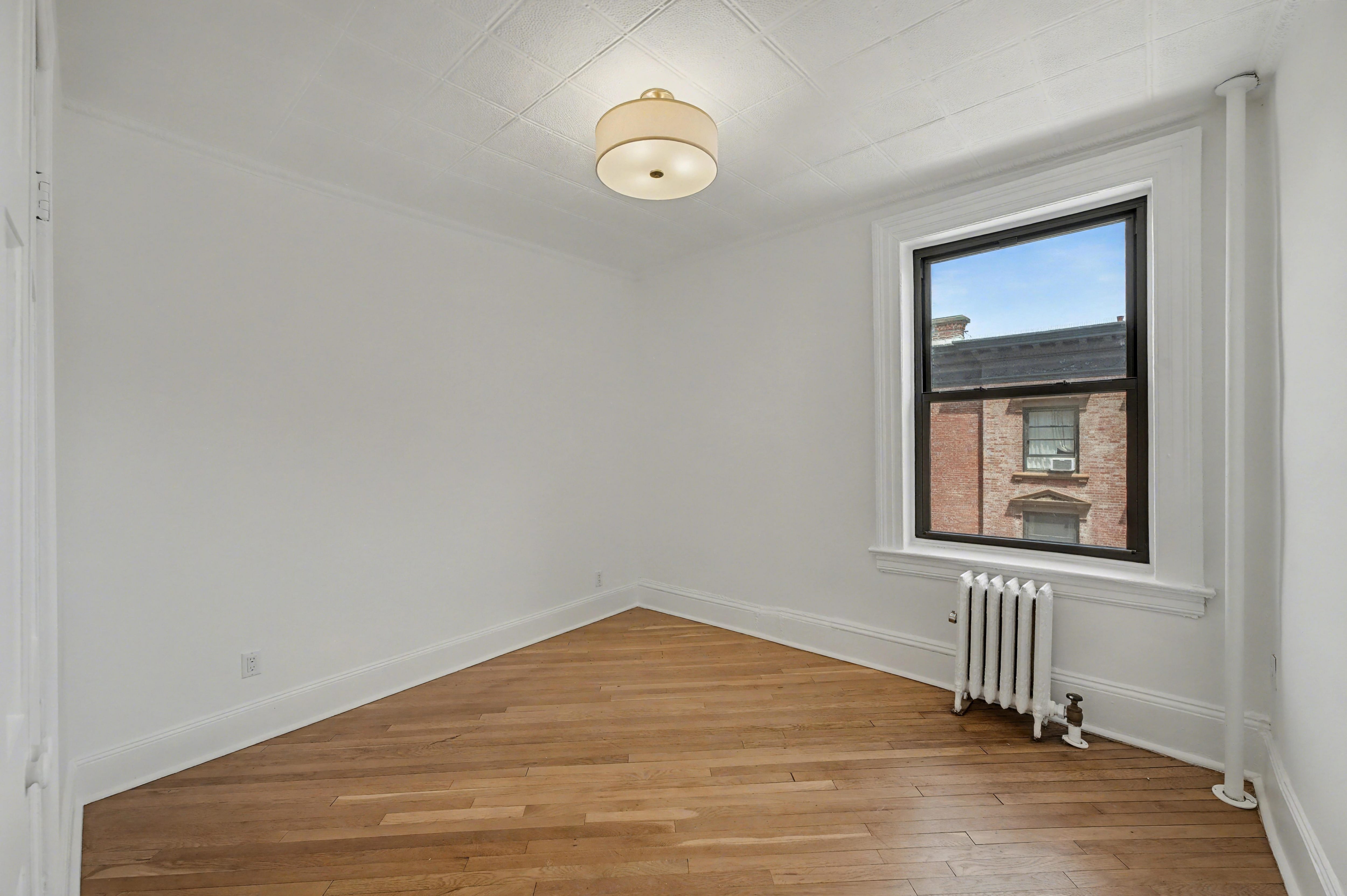 261 Clinton Street, Unit 3 Brooklyn, NY 11201 - Photo 9 of 12 a view of an empty room with wooden floor and a window